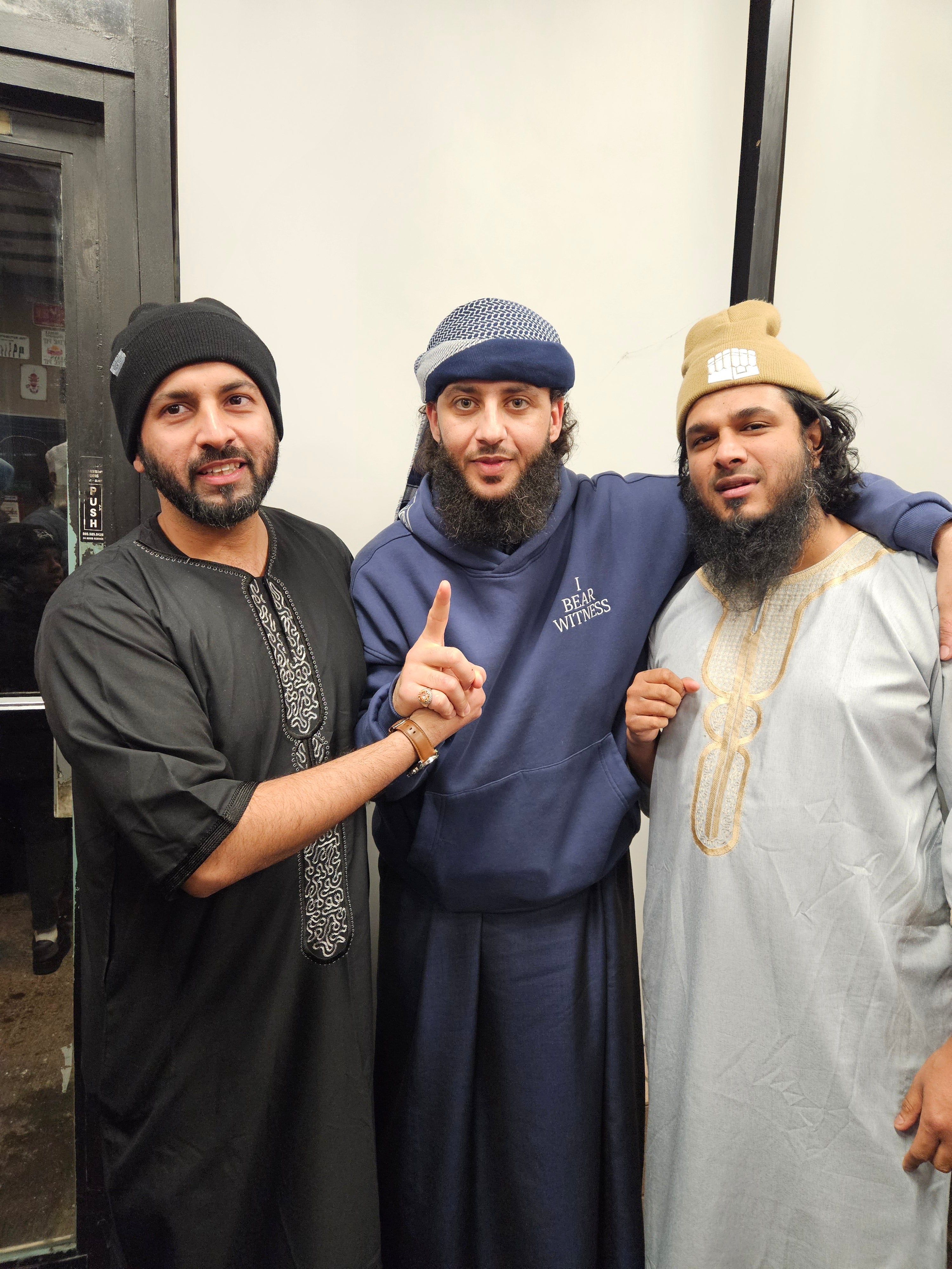 Three men posing together with a neutral background